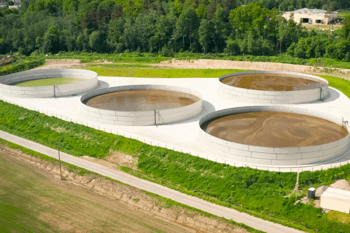 Aerial view of circular open-top biosolids storage tanks beside a road at a wastewater facility.